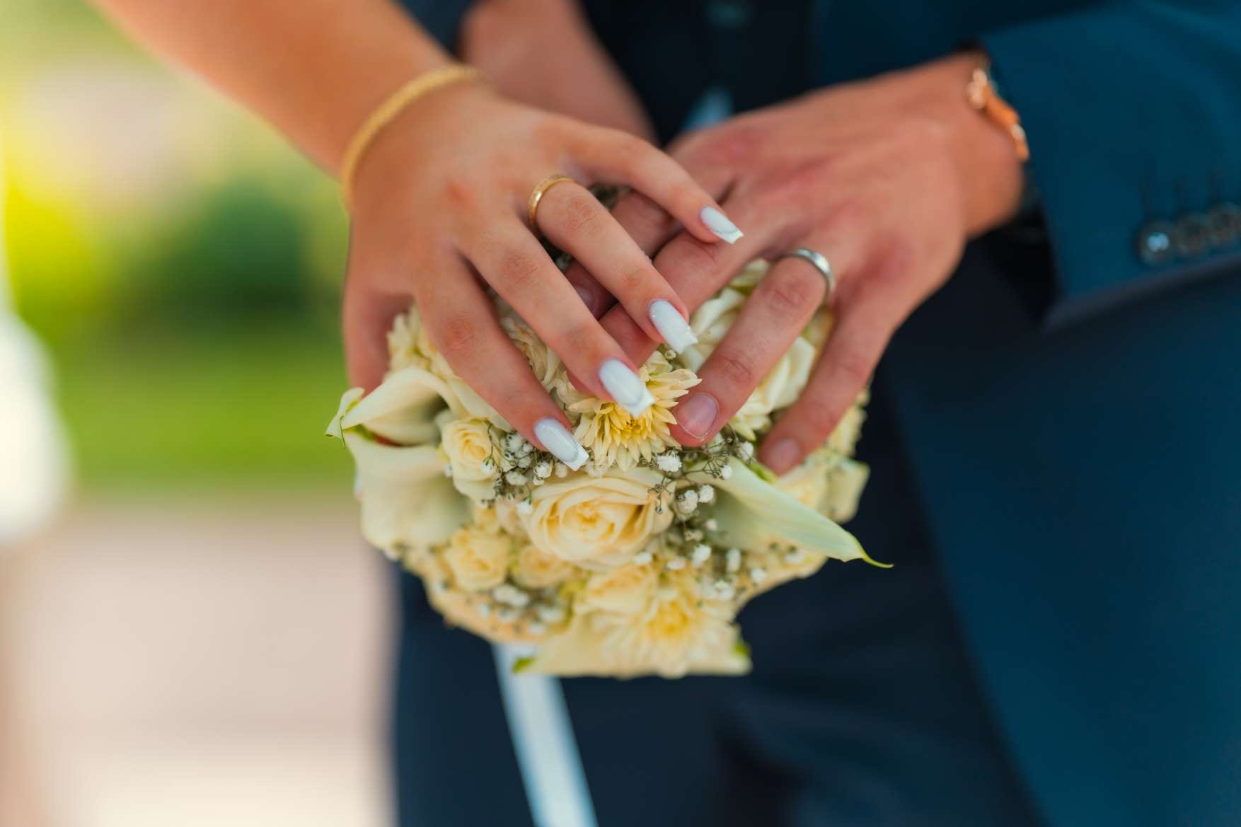 Mains des mariés réunies sur le bouquet, alliances au doigt