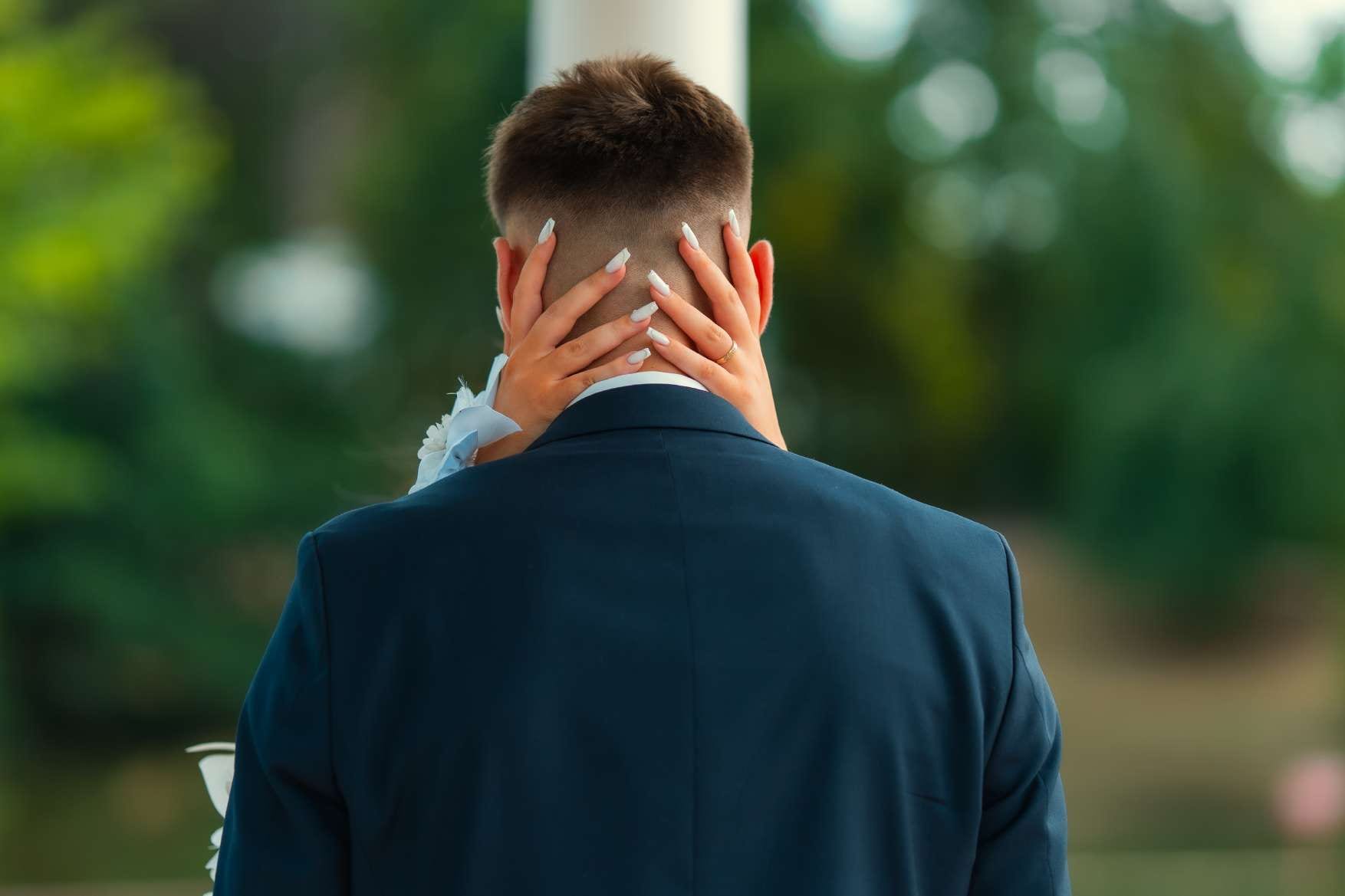 Le marié de dos, les mains de la mariée posées sur sa nuque