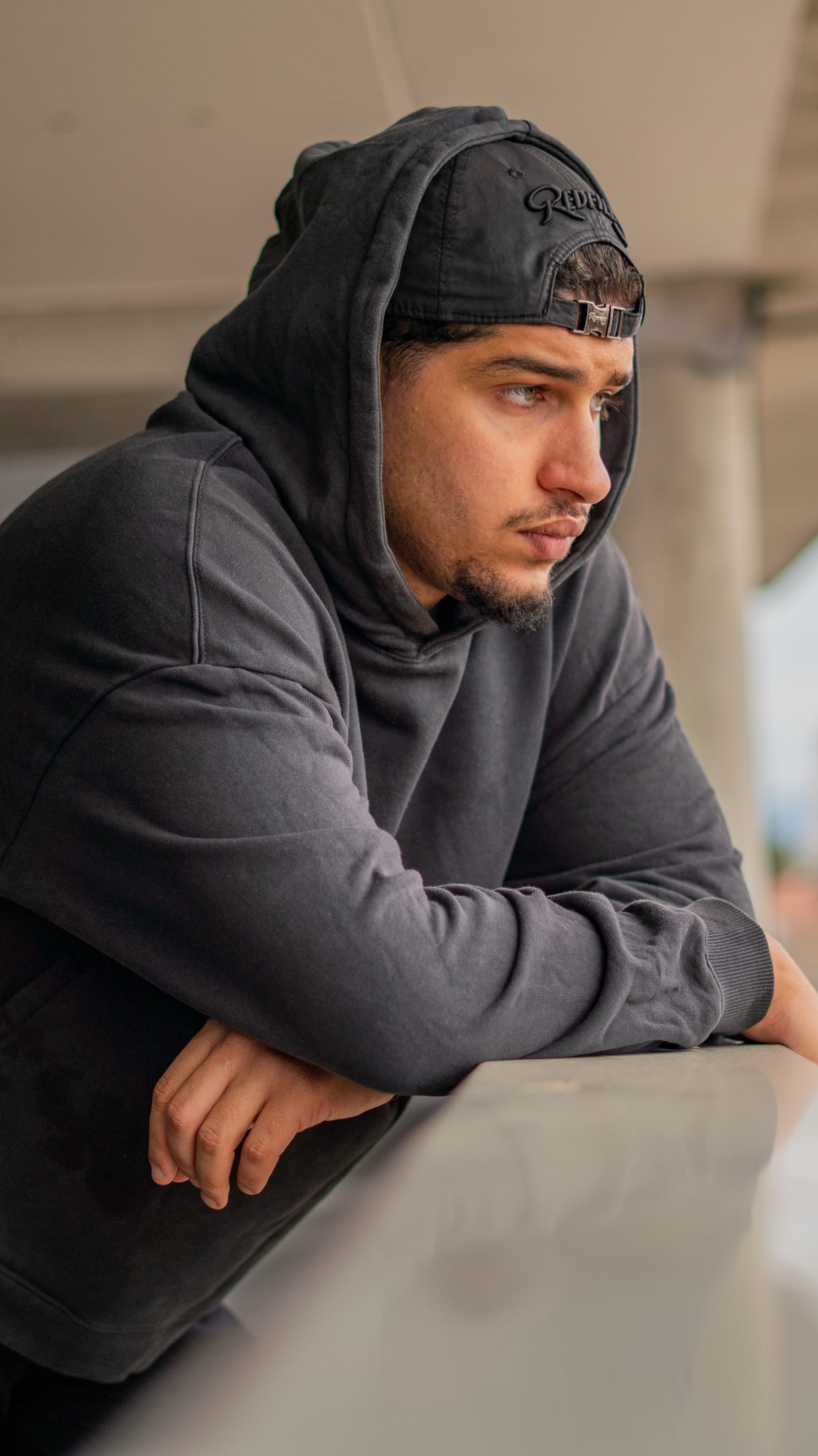 Portrait en couleur d’un homme en sweat à capuche, accoudé à une rambarde, regard au loin